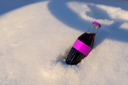 A glass bottle of soda lies in the snow in the sun raysの写真素材