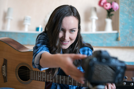 Young woman adjusts focus on the camera to record a music blog with guitarの写真素材