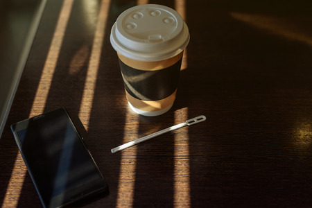 Cardboard Cup with coffee, cappuccino, latte, tea and smartphone on wooden table in cafe in bright sun rays.の写真素材