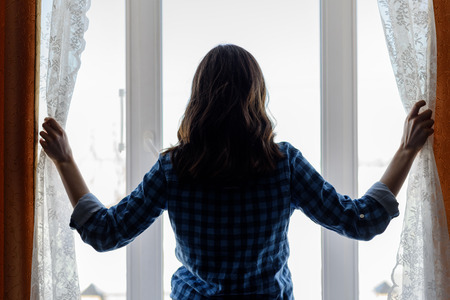 silhouette of a young woman reveals the curtains at the panoramic window
