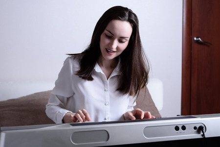 Portrait of a young woman in the interior of the room playing an electronic piano.の写真素材