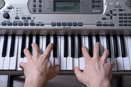 Frontal rear view of women's hands playing the keys of the electronic piano.