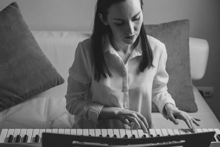 Black and white portrait of a young woman learning to play electronic piano.の写真素材