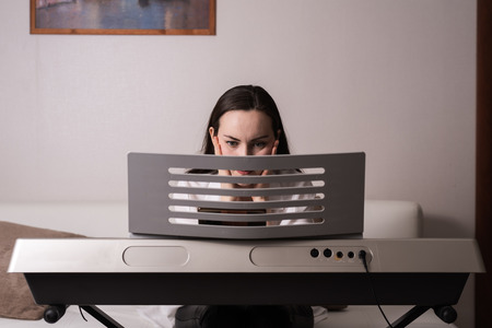 Frontal portrait of a young woman behind a synthesizer learning games through a smartphone.の写真素材