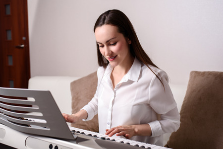 Portrait of a woman passionate about learning to play the electronic piano in the interior of the apartment.の写真素材