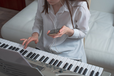 Young woman learn to play the synth using smartphone.の写真素材