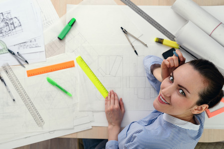 Portrait of smiling female architect on the table with drawings, rulers, pencils, compasses.