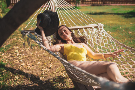 Young attractive woman in yellow swimsuit resting in a hammock under a tree.の写真素材