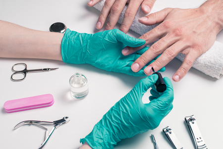 Men's manicure. Beautician in rubber gloves, apply a protective nail Polish.の写真素材