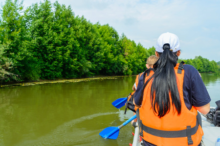 Woman in a cap and an orange life jacket works as a paddle on an inflatable catamaranの写真素材