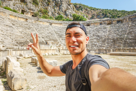 Selfie of a young man in a cap, shows the symbol of peace on the background of the amphitheater. Travel, adventure emotionsの写真素材