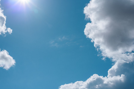 Abstract background of blue sky with lush clouds and bright rays of the sun with a copy of space.