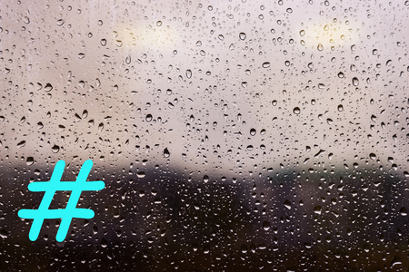 Water drops from rain on the window glass against the urban landscape, with a hashtag.の写真素材