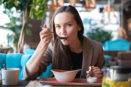 Portrait of a young woman in the interior of the restaurant at the table eating soup with bread, blurred background.の写真素材