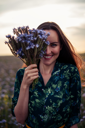 Happy smiling woman covers the floor of her face with bouquet of purple flowers close-upの写真素材