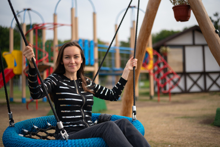 Portrait of a young woman swinging on a hanging swing smiling, concept of freedom, day off, remember childhood.の写真素材