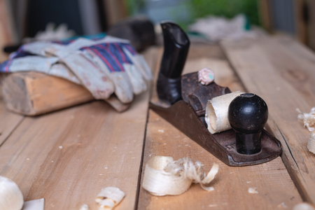 Old retro hand planer with gloves and mallet on wooden table with sawdust and shavings. carpentry,...