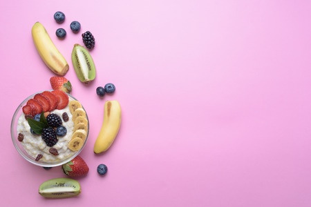 flat lay of oatmeal with berries and fruits in glass bowl on pink background with copy space....