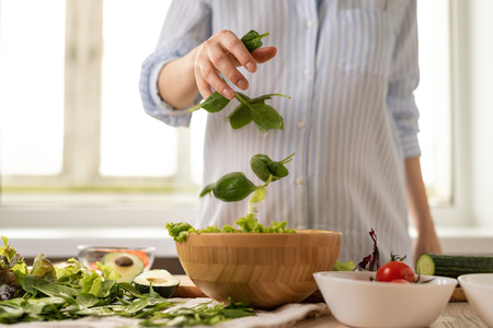 close up pregnant woman in blue shirt cooking salad with motion effect. process of cooking vegetable salad conceptの写真素材