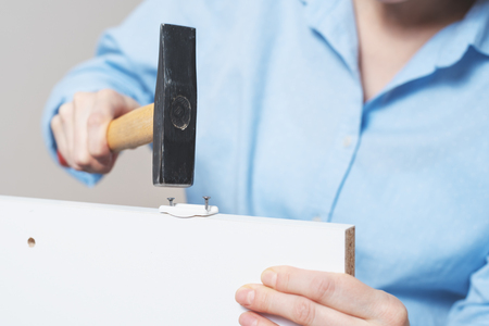 housewife in blue shirt hammering nail with hammer, concept of furniture Assembly, close upの写真素材