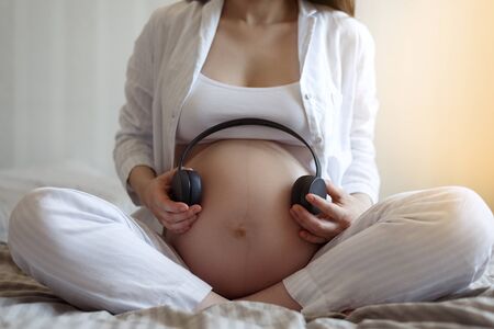 Music for pregnant. close-up of pregnant woman with wireless headphones applies to tummy, baby development.の写真素材