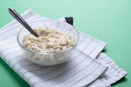 Food minimalism. Porridge oatmeal in pink plate with spoon on green background with copy space.の写真素材