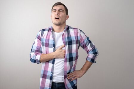 Portrait of a sickly man holding his heart on a gray background. heart disease