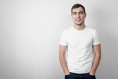 Authentic portrait of caucasian smiling young man in white blank t-shirt with copy space on grey backgroundの写真素材