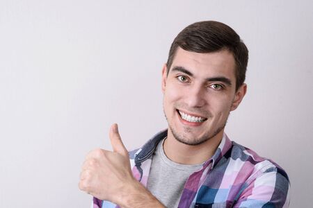 Smiling Caucasian man looking at camera and showing thumb up over gray background with copy space