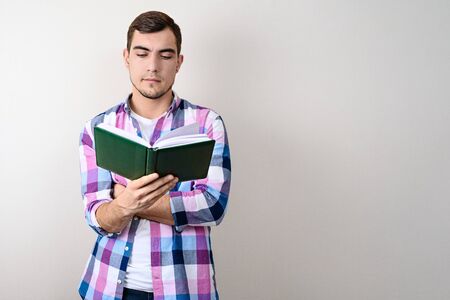 Young Caucasian male student in plaid shirt reading book on grey background with copy spaceの写真素材