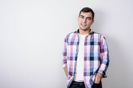 Portrait of modern European young man in pink plaid shirt and white t-shirt against gray wall with copy spaceの写真素材