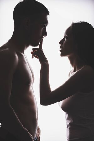 Silhouette of a young couple, the woman covers her mouth with finger men, women powerの写真素材