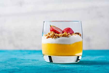 Frontal one glass with a dessert of mango, yogurt, mussels and strawberries, on a turquoise background with copy spaceの写真素材