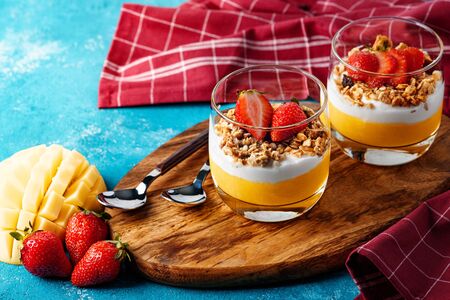 delicious and healthy Breakfast with mango, granola, cottage cheese and strawberries on wooden Board on blue backgroundの写真素材