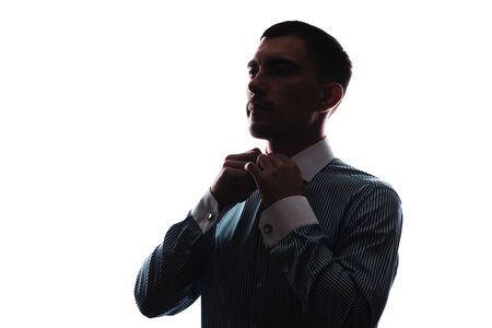 silhouette of Young European man buttoning his shirt collar on white background, side viewの写真素材