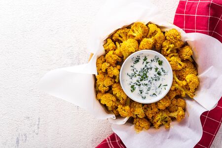 vegetarian baked cauliflower with breadcrumbs and spices with sour cream sauce and greens on white background. vegetarian snack conceptの写真素材