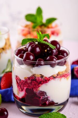 close up vertical image of dessert with cherries, whipped cream, granola and mint on light pink background. trifle conceptの写真素材