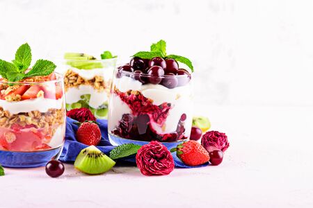 trifles with cherries, strawberries, kiwi, whipped cream and granola in glass on blue napkin on light pink background with copy space. berry dessert conceptの写真素材