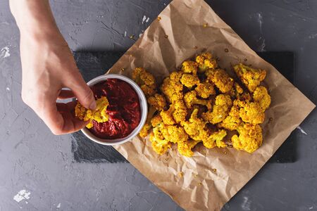hand waving cauliflower in tomato sauce on black stone Board on gray background, top viewの写真素材