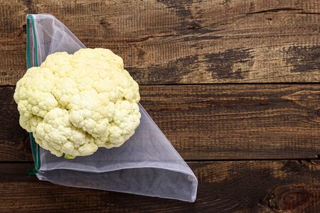 Fresh cauliflower in reusable eco-friendly pouch on wooden background with copy space, eco food conceptの写真素材
