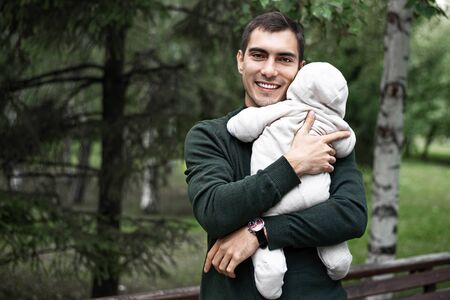 smiling father brunette in green jacket with baby in his arms on walk in the Park with copy space