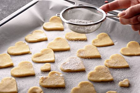 close up cookies hearts on parchment paper on baking sheet sprinkle powdered sugar on top through...