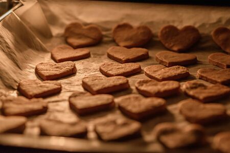 close up baking homemade cookies hearts on white parchment paper in the ovenの写真素材