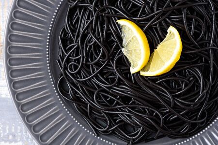 closeup black spaghetti with ink cuttlefish with lemon on gray plate on gray background with copy space, black pasta conceptの写真素材