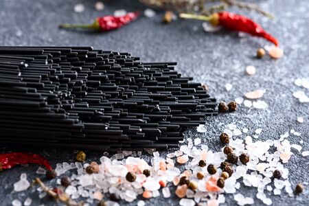 close-up of black paste with cuttlefish ink with chili pepper sprinkled with pink salt and peppercorns on grey kitchen table, black spaghetti conceptの写真素材