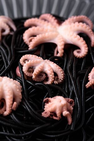 vertical closeup trendy black pasta with cuttlefish ink with octopuses in grey plateの写真素材