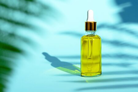 trendy dropper glass bottle with yellow cosmetic oil on blue background and leaf shadowの写真素材