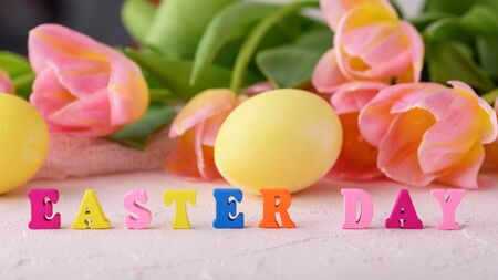 Easter concept, closeup colorful wooden letters easter day on background of tulips and Easter eggsの写真素材
