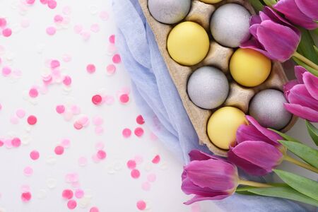 top view festive Easter composition of purple tulips and yellow and blue Easter eggs with pink...