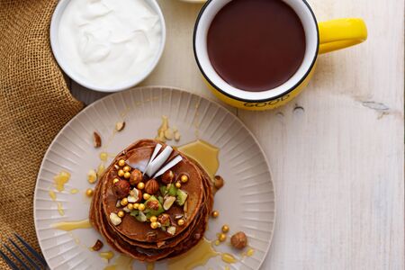 top view chocolate pancakes with kiwi, hazelnut, honey on plate with sour cream and cup of cocoa on white backgroundの写真素材